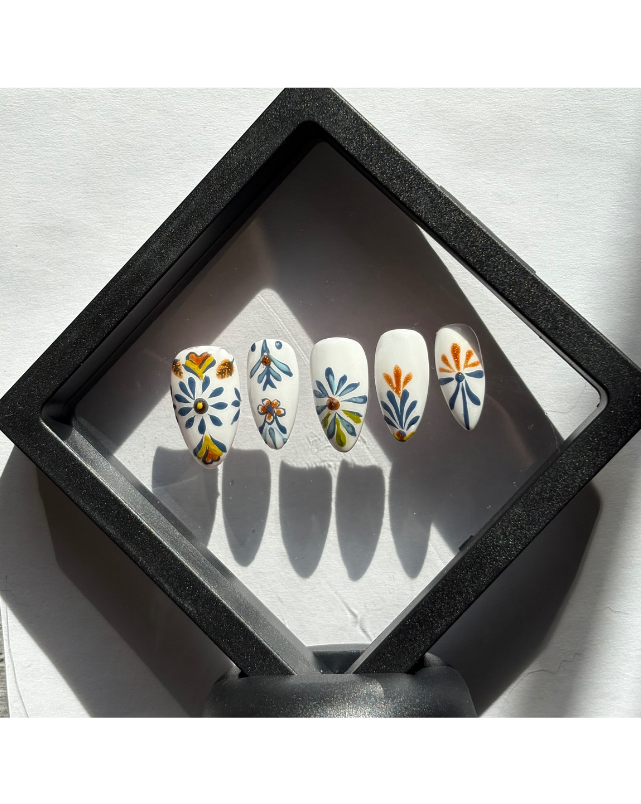 Inspired by traditional Mexican Talavera pottery. Hand-painted with intricate blue and marigold floral motifs on a crisp porcelain-white base. Each nail is hand-painted with cobalt blue and golden-orange motifs. The designs feature symmetrical floral elements and geometric borders found in authentic Talavera pottery.