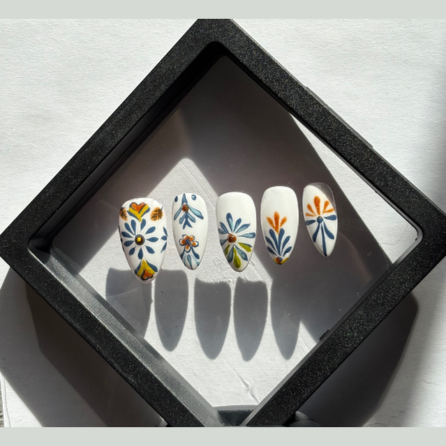 Inspired by traditional Mexican Talavera pottery. Hand-painted with intricate blue and marigold floral motifs on a crisp porcelain-white base. Each nail is hand-painted with cobalt blue and golden-orange motifs. The designs feature symmetrical floral elements and geometric borders found in authentic Talavera pottery.