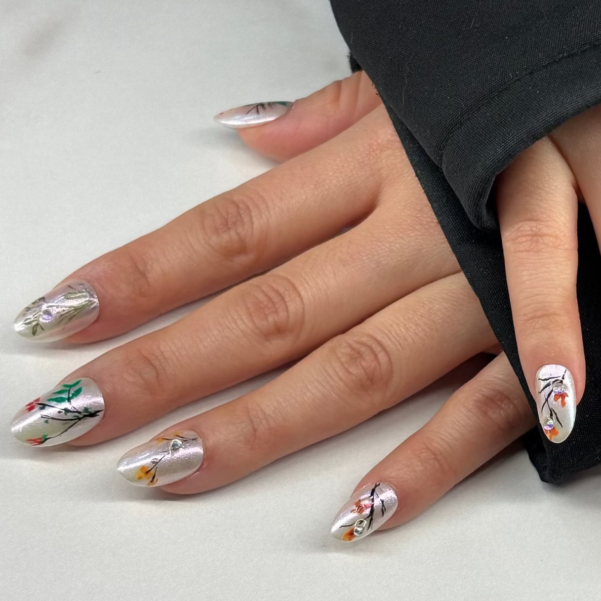 A milky white base with pearl finish gives it the muse of a Chinese garden. We’ve hand-painted thin, dark stems and small colorful buds across the nails to mimic early spring growth. A few small crystals are added to catch the light, like water droplets. It’s a simple, honest design for those who want a professional look that feels light and seasonal.
