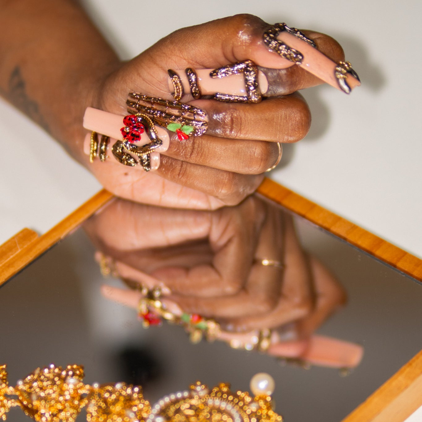 Hand showing ornate, long square shaped nails with 3D gold chrome work that is opulent and looking like hoops and ornate jewelry.