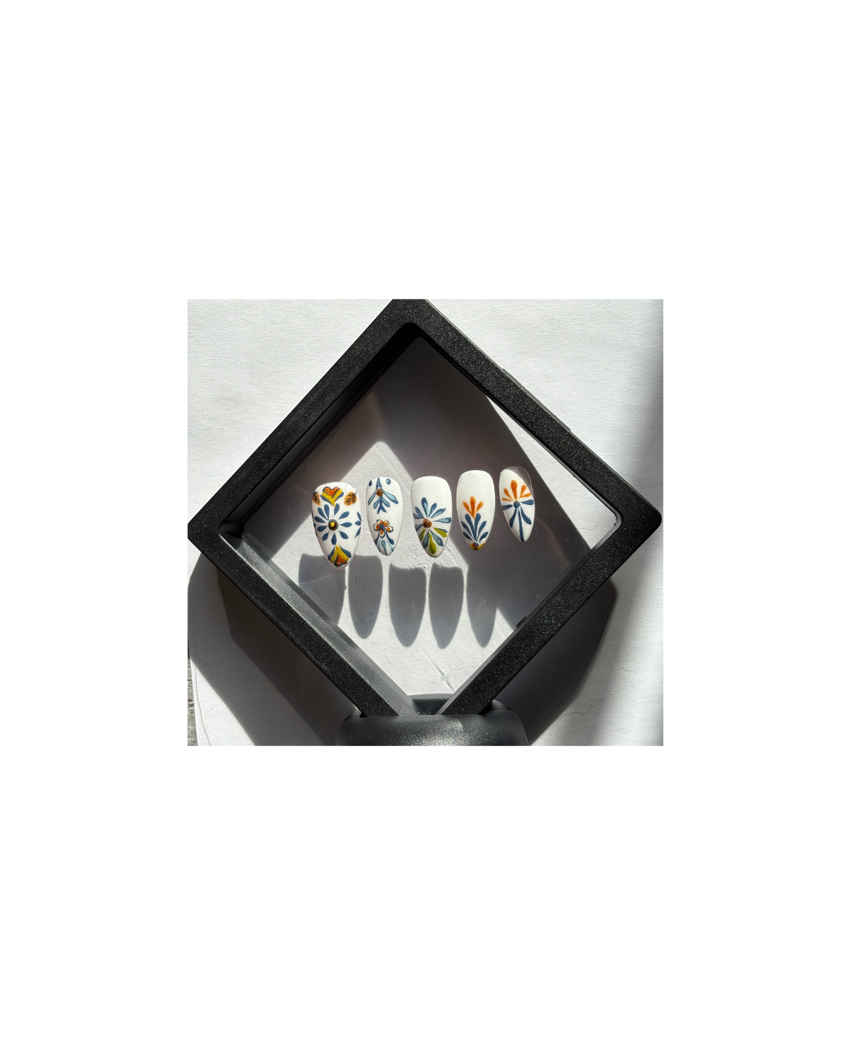 Inspired by traditional Mexican Talavera pottery. Hand-painted with intricate blue and marigold floral motifs on a crisp porcelain-white base. Each nail is hand-painted with cobalt blue and golden-orange motifs. The designs feature symmetrical floral elements and geometric borders found in authentic Talavera pottery.