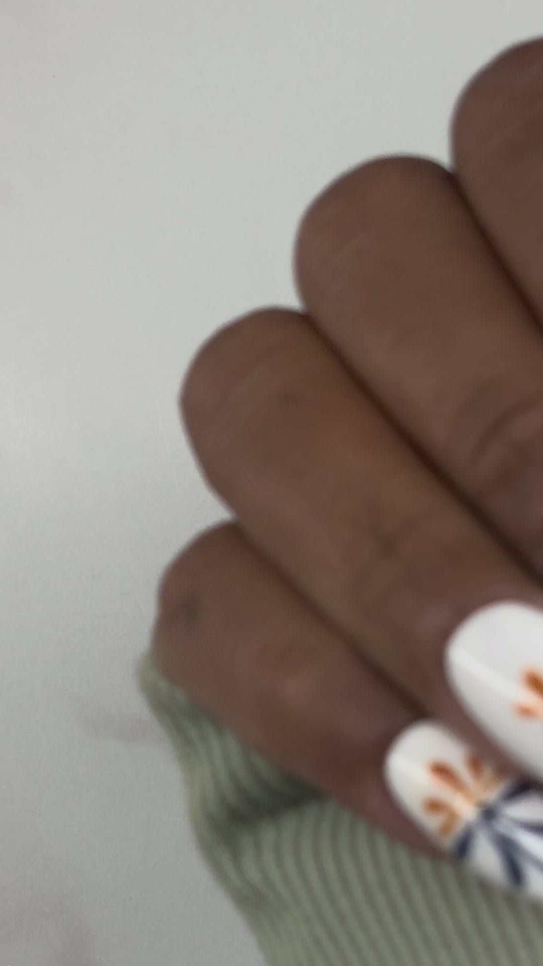 Hands displaying white nails with intricate line work displaying Mexican Telavara art