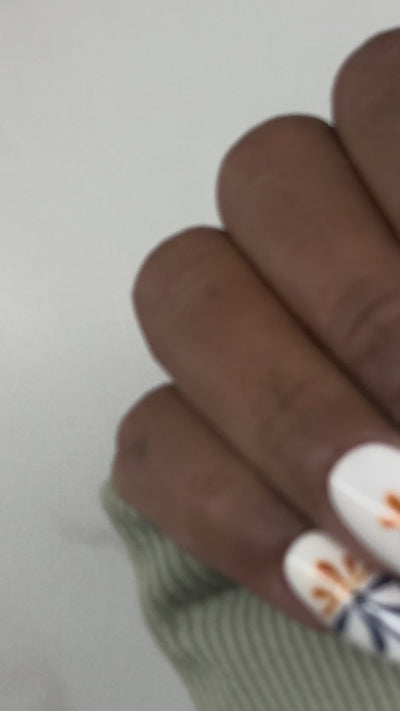 Hands displaying white nails with intricate line work displaying Mexican Telavara art